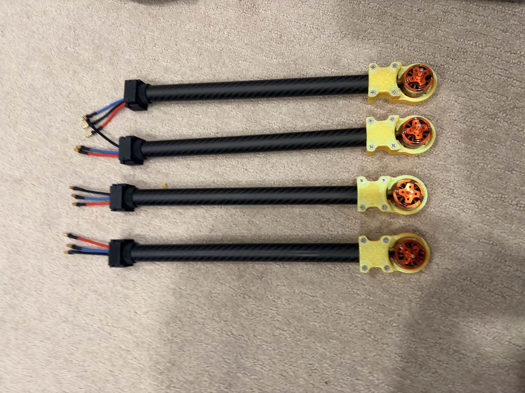 Four carbon-fiber arm assemblies with yellow 3D-printed motor mounts and installed brushless motors.